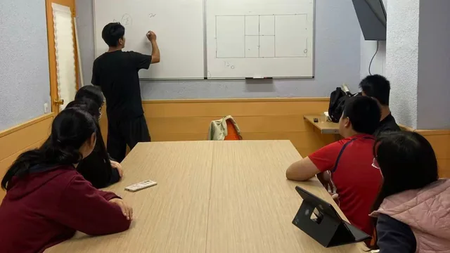 Un profesor explica en la pizarra mientras los alumnos toman notas.